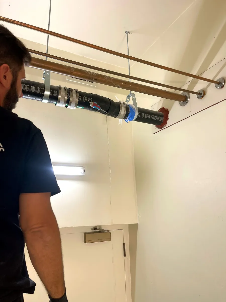 Plumber working on a drain line in a building hallway ceiling in Palo Alto
