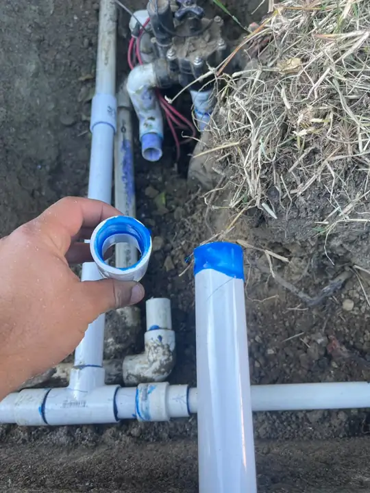 Plumber holding a new PVC coupling for an irrigation pipe repair